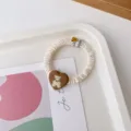 White pleated hair scrunchie featuring a brown heart charm with a cute bear and fabric tag. - Milky White Scrunchie + Brown Body Bear Cloth Label