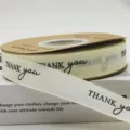 Beige ribbon roll with black thank you print, ideal for gift wrapping and party decor. - Thank You Style