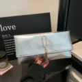 Detailed view of silver metallic envelope clutch bag, highlighting sleek gold ring and tassel. - Silver