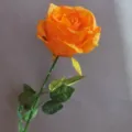 Primer plano detalle de flor de rosa naranja artificial con tallo verde, decoración hogar. - Naranja