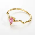 Detailed closeup of a golden wavy ring with a sparkling pear-shaped pink zirconia stone. - Gold Style 8