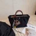 Versatile black nylon crossbody handbag featuring brown leather handles and chic charms. - Black
