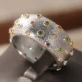 Primo piano dettagliato di un anello largo argentato strutturato con pietre colorate. - Taglia 6 / Due colori