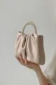 Close-up detail of stylish pleated beige handbag with elegant faux pearl handle design. - Pink