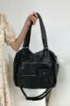 Detailed view of large capacity black motorcycle style multi pocket tote shoulder bag. - Black