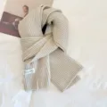 Beige knitted scarf detail shot showing soft ribbed texture and neat brand label design. - Cappuccino