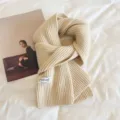 Detailed shot of beige knitted winter scarf showing soft wool texture and elegant brand label. - Milky Apricot