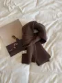 Detailed close-up of a dark brown knitted winter scarf with ribbed texture and tag. - Coffee