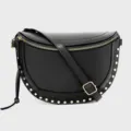 Close-up detail of black leather crescent crossbody bag with gold studs and zipper hardware. - Black