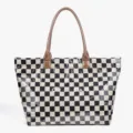 Detail view of the black and white checkered PVC tote bag with brown leather handles. - Checkerboard Brown