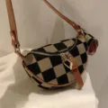 Close-up of stylish black and tan checkerboard canvas crossbody bag with brown leather strap. - Sand Yellow