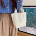 Detailed close-up view of a minimalist canvas tote bag, compact lunch handbag storage. - Metal Snap Closure / White