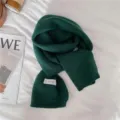 Vue détaillée de l'écharpe en tricot vert foncé, montrant la texture douce et une étiquette. - Vert Feuille de Lotus