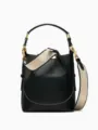 Detail shot of black leather bucket bag with wide beige shoulder strap and brass hardware. - S / Black
