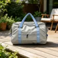 Vista dettagliata di una borsa da viaggio grigia con manici blu su una terrazza in legno. - Blu