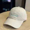 Detail shot of the beige cotton baseball cap featuring blue formed embroidery and classic brim. - Beige