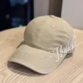 Detail view of a khaki baseball cap featuring stylish white cursive embroidery on the side. - Adult 54-60 Adjustable / Khaki