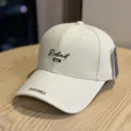 Detailed close-up of beige embroidered baseball cap with stylish text on curved brim. - Adult 54-60 Adjustable / Beige
