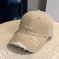 Detailed view of the vintage distressed baseball cap with white cursive embroidery and ripped brim. - Adult 54-60 Adjustable / Khaki