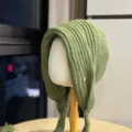 Detailansicht einer kuscheligen grünen Strickmütze mit Ohrenklappen und Metall-Logo. - Erwachsene 54-60 Einheitsgröße / Olive