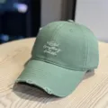 Detail view of the light green washed baseball cap featuring distressed brim and text embroidery. - Adult 54-60 Adjustable / Olive