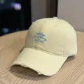 Light yellow washed cotton baseball cap detail with distressed brim and blue embroidered text. - Adult 54-60 Adjustable / Yellow
