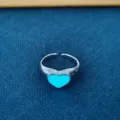 Close-up detail van de stijlvolle open legeringsring met een gloeiend blauw hartelement. - Lichtgevend Blauwgroen