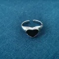 Gedetailleerde close-up van een stijlvolle open zilveren ring met een glanzend zwart hart. - Zwart