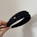 Primo piano di un cerchietto nero a pois bianchi in tessuto, consistenza e dettaglio dorato. - Cerchietto Concavo-Convesso a Pois Nero / Nero