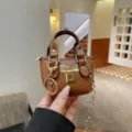 Mini brown leather crossbody handbag closeup showing luxury style metal lock and chain strap details. - Brown