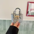 Detailed shot of mini blue leather handbag charm with gold hardware, padlock and handle design. - Blue