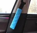 Detailed close-up view of a soft blue plush car seatbelt cover with embroidered pattern. - Blue