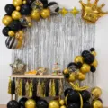 Birthday party balloon decoration set with black gold balloons and silver fringe curtain backdrop. - Black Balloon Garland