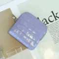 Primer plano de un monedero de cuero morado con relieve de cocodrilo y cremallera plateada. - Púrpura de ensueño