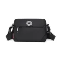 Black nylon crossbody bag detail showing metallic front badge, zipper pocket, and strap. - S / Black