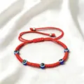Vue détaillée du bracelet tressé rouge avec mauvais œil et perles de protection bleues. - Cinq Yeux (Corde Rouge)