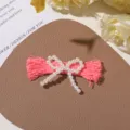 Detailed close-up of a DIY handmade pink tassel hair clip decorated with white pearls. - Pink