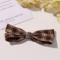 Detail view of brown plaid hair bow featuring a metallic cross charm and neat fabric texture. - L / Brown