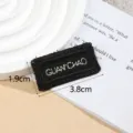 Black embroidered woven label detail view, featuring silver lettering and precise fabric texture. - GUANCHAO / Black