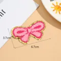 Close-up van roze strik borduurpatch met gouden glitterrand en 3.7x6.7cm maatinformatie. - Stijl 3