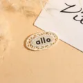 Close-up detail of oval lace embroidered woven clothing label patch with clean design. - Oval / Beige