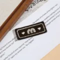 Nahaufnahme des braunen bestickten Buchstabenaufnähers mit Herzdetails auf Buchseite. - Spezifikation Eins (4.7x1.7cm)