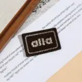 Detailansicht eines bestickten Buchstaben-Aufnähers, brauner Stoff mit weißer Stickerei. - Spezifikation Zwei (4.3x2.8cm)