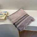 Detailed close-up of folded pink knitted scarf with striped pattern and fringe edges. - Pink