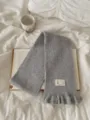 Grey knitted scarf with elegant ruffle trim and cozy texture, detailed shot of winter accessory. - Gray
