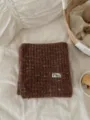 Close-up detail of cozy brown multi-color knitted scarf with brand label, soft winter texture. - Coffee