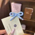 Close-up detail of a cute blue polka dot bow hair clip displayed on a branded card. - Blue