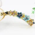 Gros plan détaillé d'une pince à cheveux banane en métal doré avec fleurs en émail bleu et strass. - Bleu