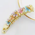 Nahaufnahme einer goldenen Bananenhaarspange mit bunten Emaillblumen und klaren Kristallen. - HB00738 / bunt
