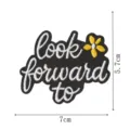 Schwarzer Stickaufnäher mit inspirierender Aufschrift look forward to und kleiner gelber Blume. - look forward to